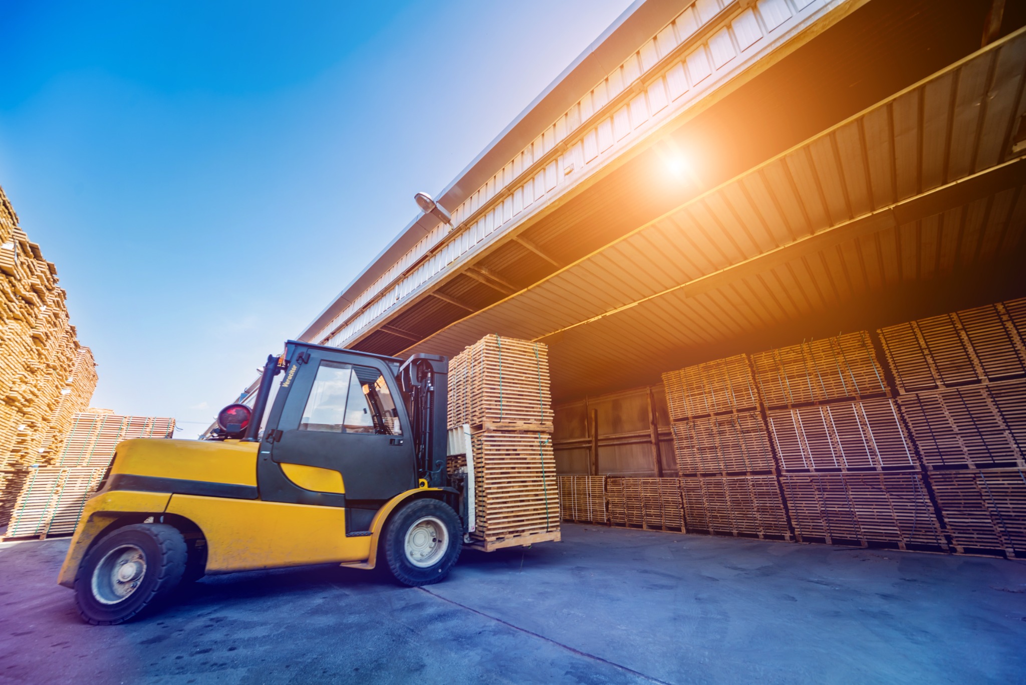 Forklift handling stacked timber beside a warehouse